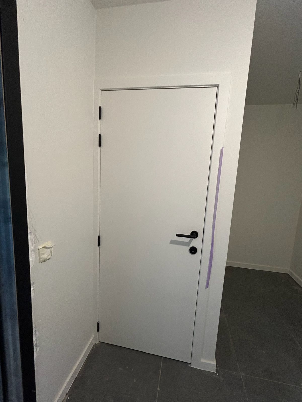 Witte binnendeur met zwarte klink in een afgewerkte hal van een woning in De Pinte.