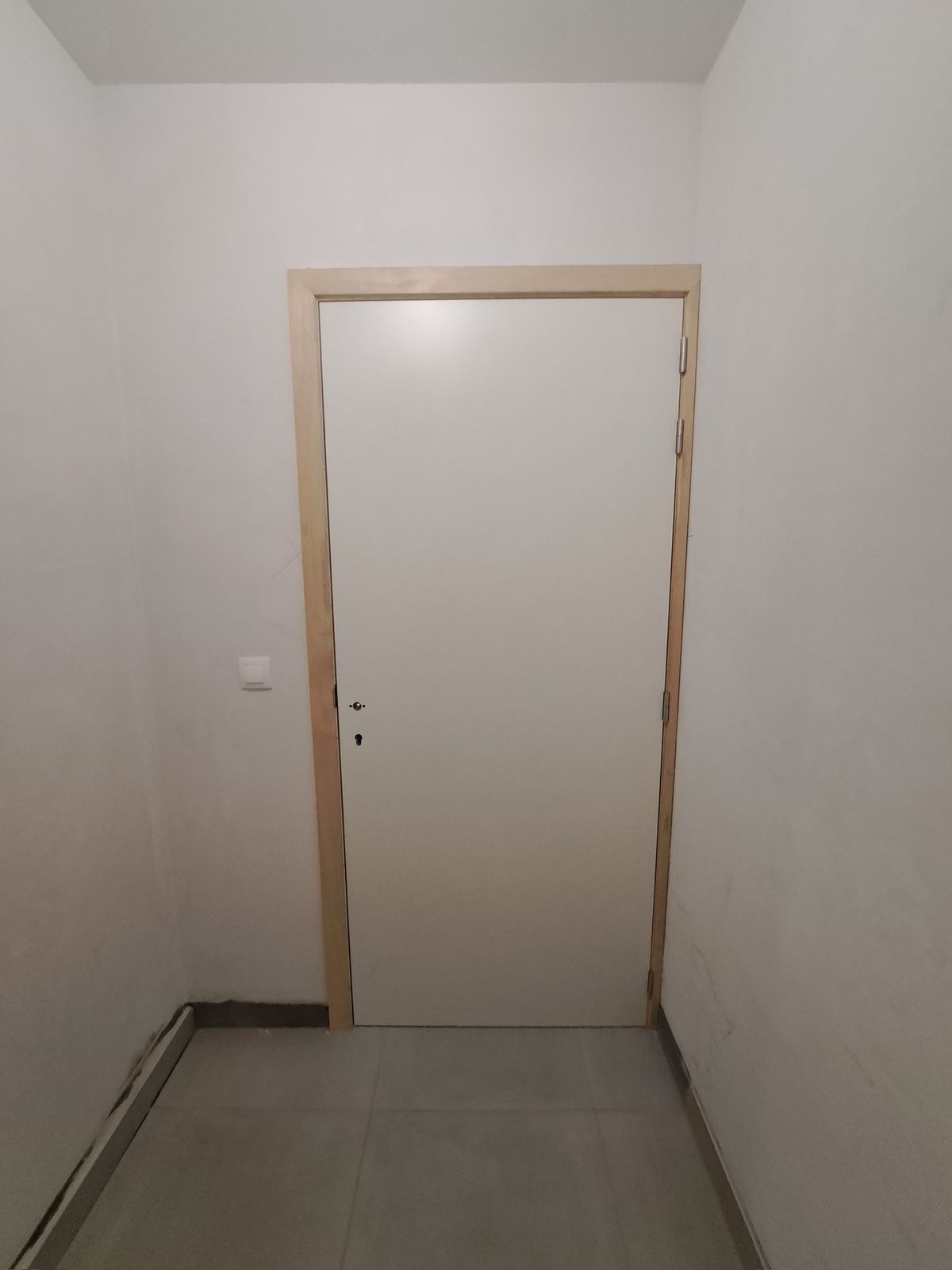 Witte binnendeur met houten deurkader in een gang met tegelvloer in Hamme.