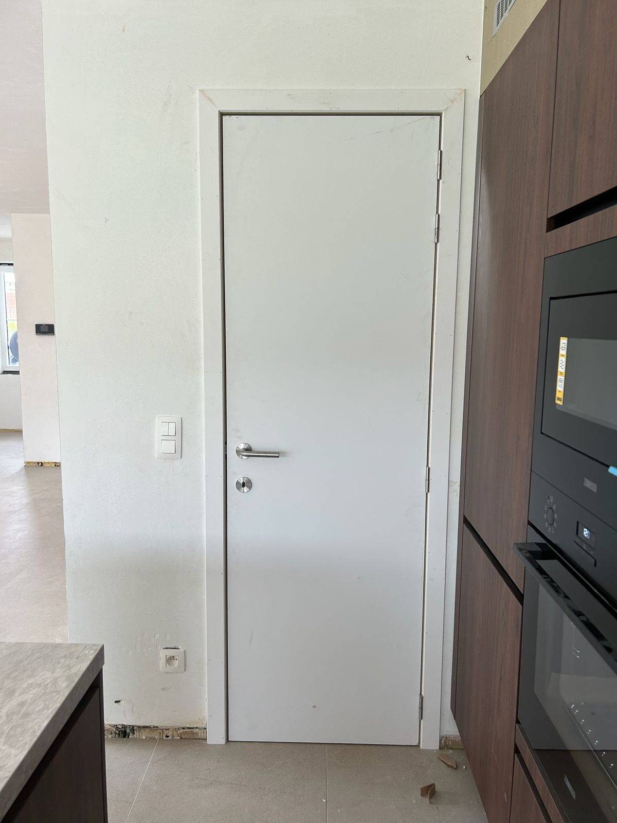 Witte binnendeur naast een donkere keukenwand met inbouwtoestellen in Wildenburg.