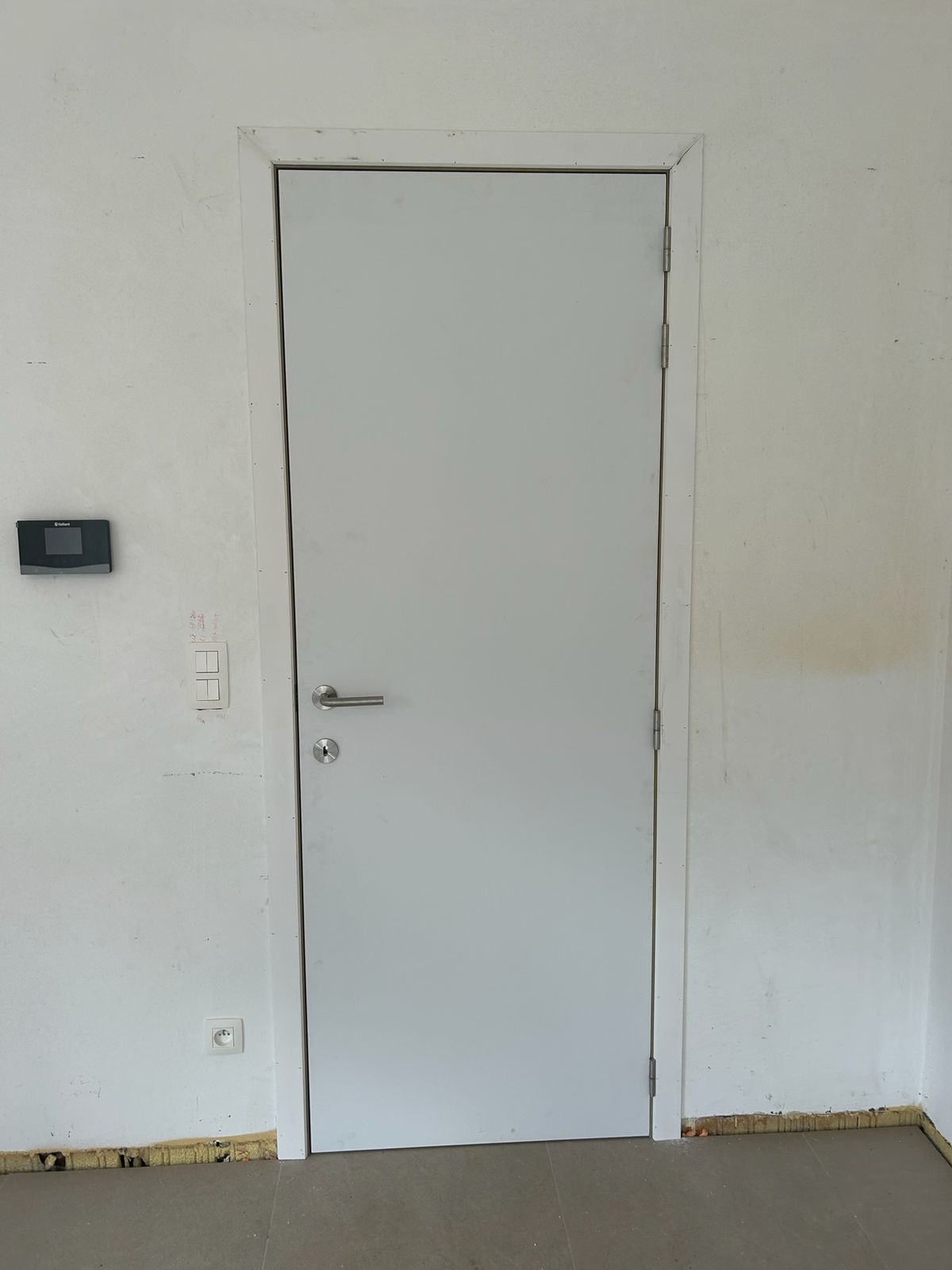 Witte binnendeur met slanke omlijsting in een witte muur in Wildenburg.