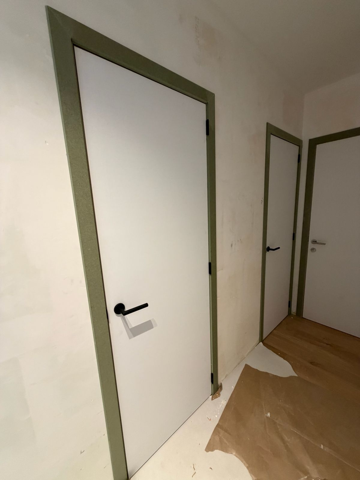 Witte binnendeuren met groene deurkaders en zwarte klinken in een gang in Nieuwpoort.