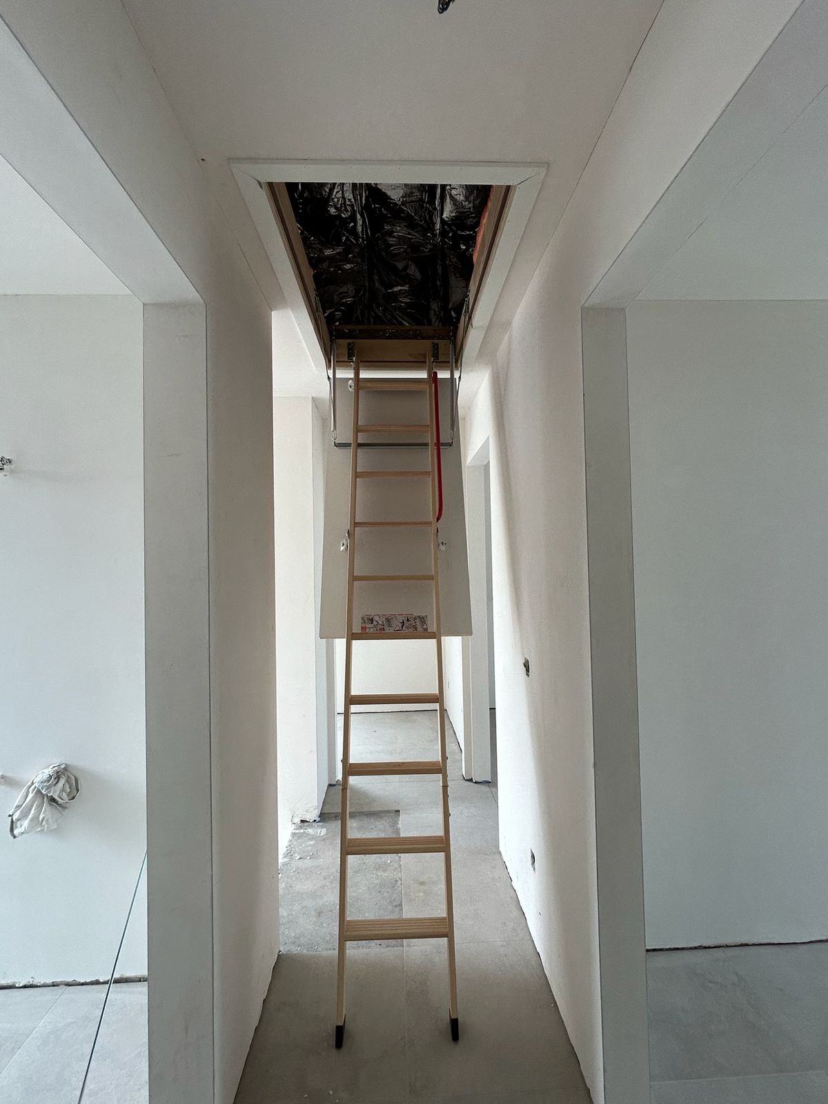 Uitgeklapte zoldertrap onder een zolderluik in een gyproc plafond van een gang in Vlissegem.