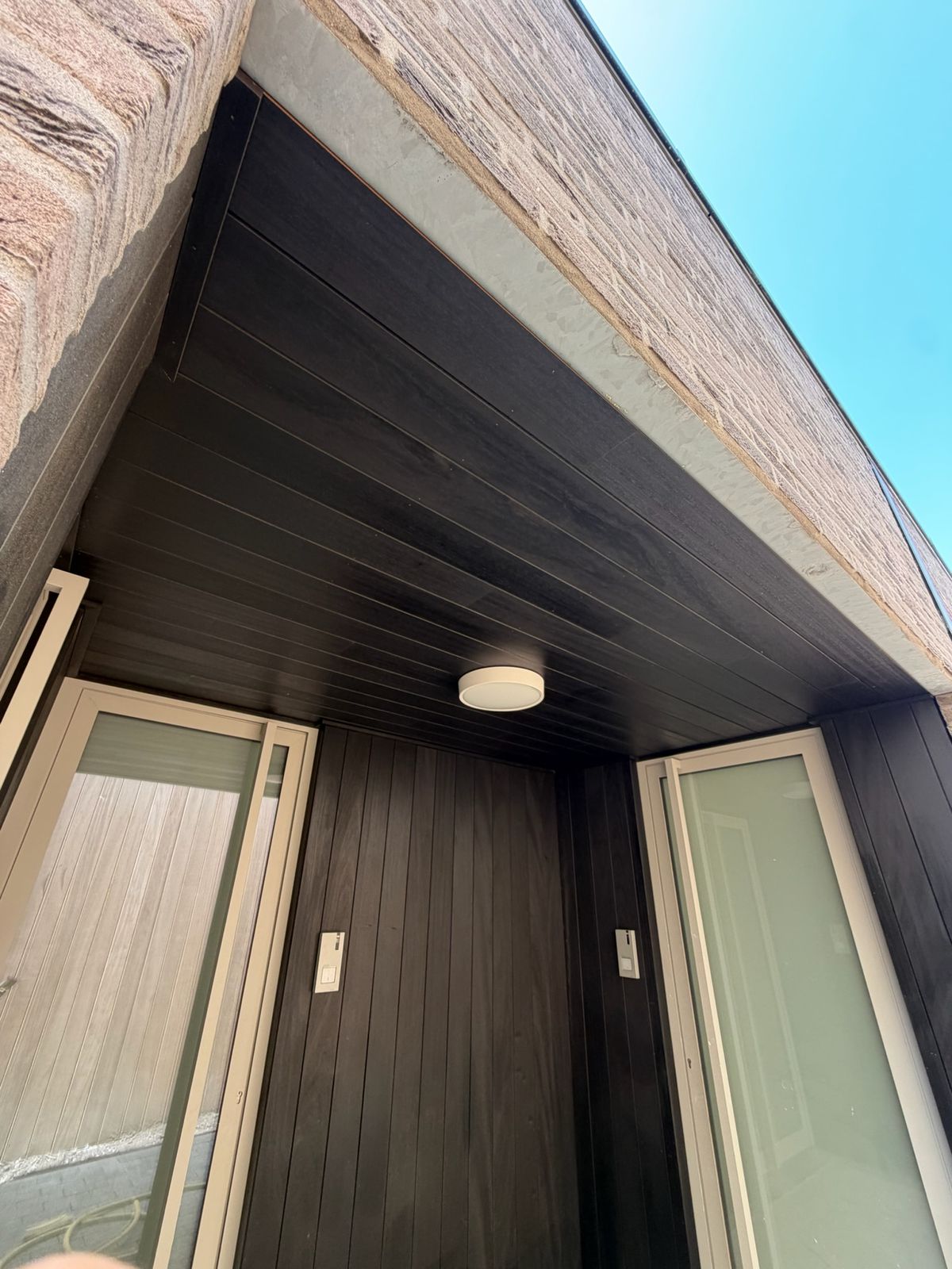 Zwart houten buitenplafond met inbouwspot boven een loggia met twee glazen deuren in Sint-Kruis.