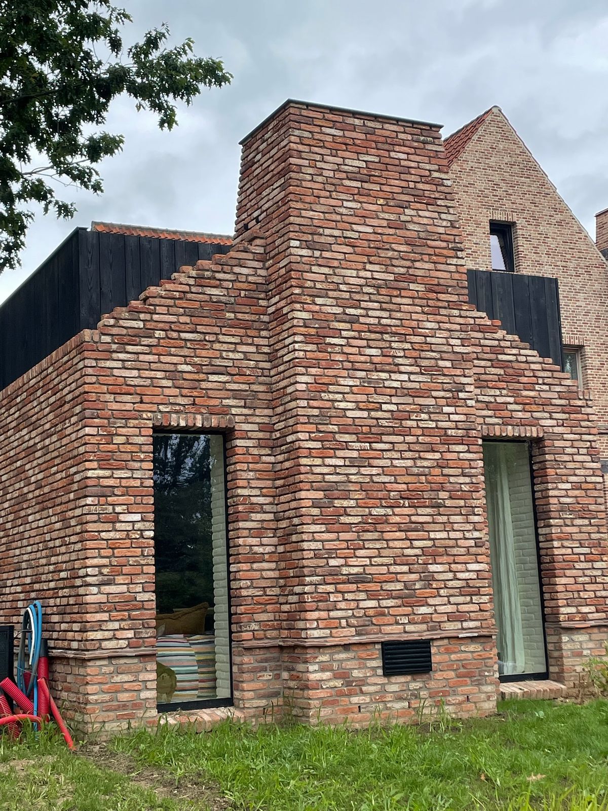 Woning in rode baksteen met zwarte houten gevelbekleding naast de schoorsteen in Meise.