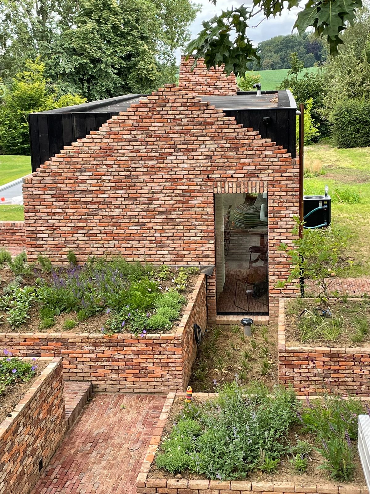 Bakstenen woning met zwarte houten gevelbekleding en tuin met plantenbakken in Meise.