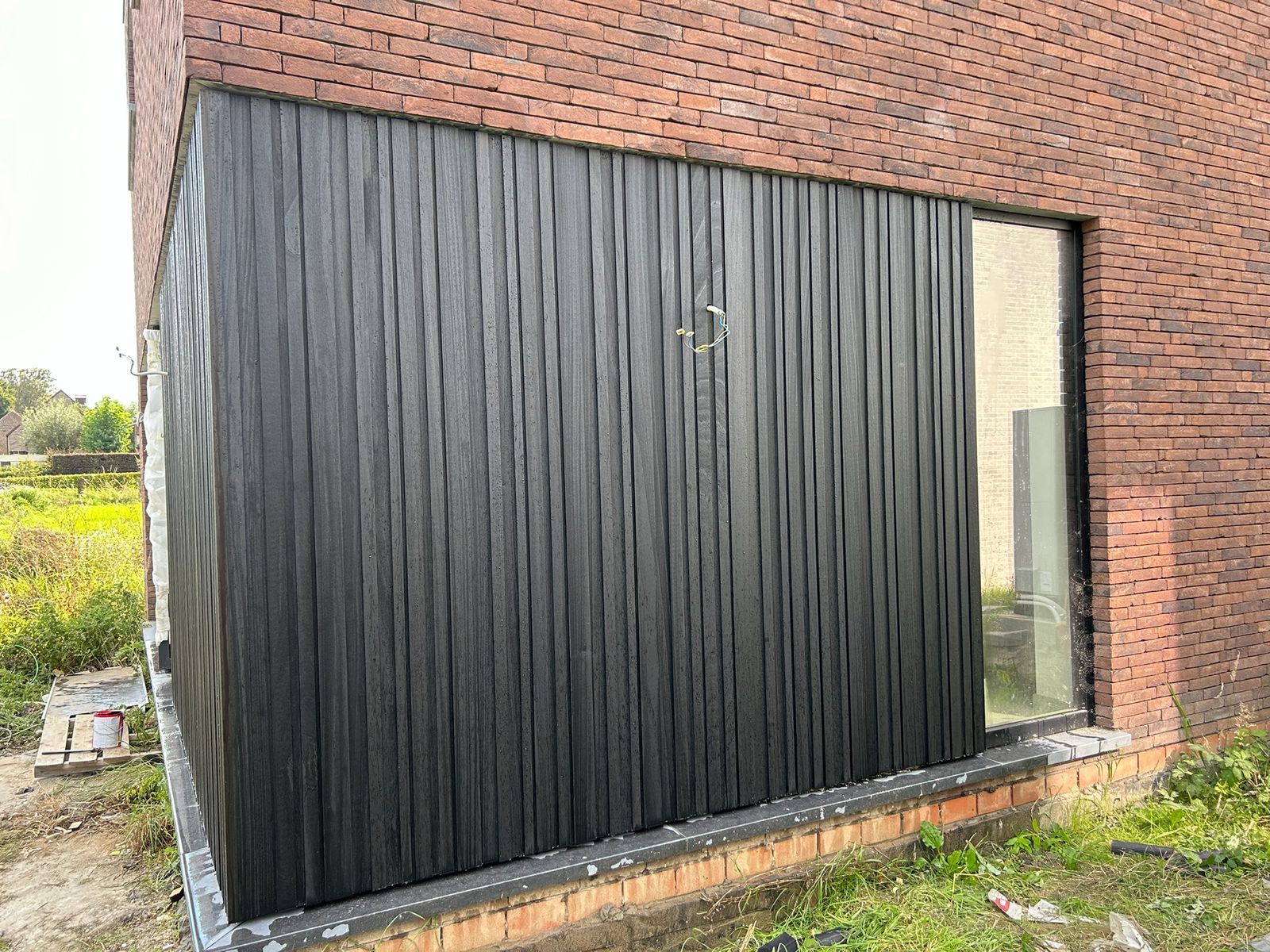 Detail van zwarte verticale gevelplanken naast een raam aan een woning in Wambeek.