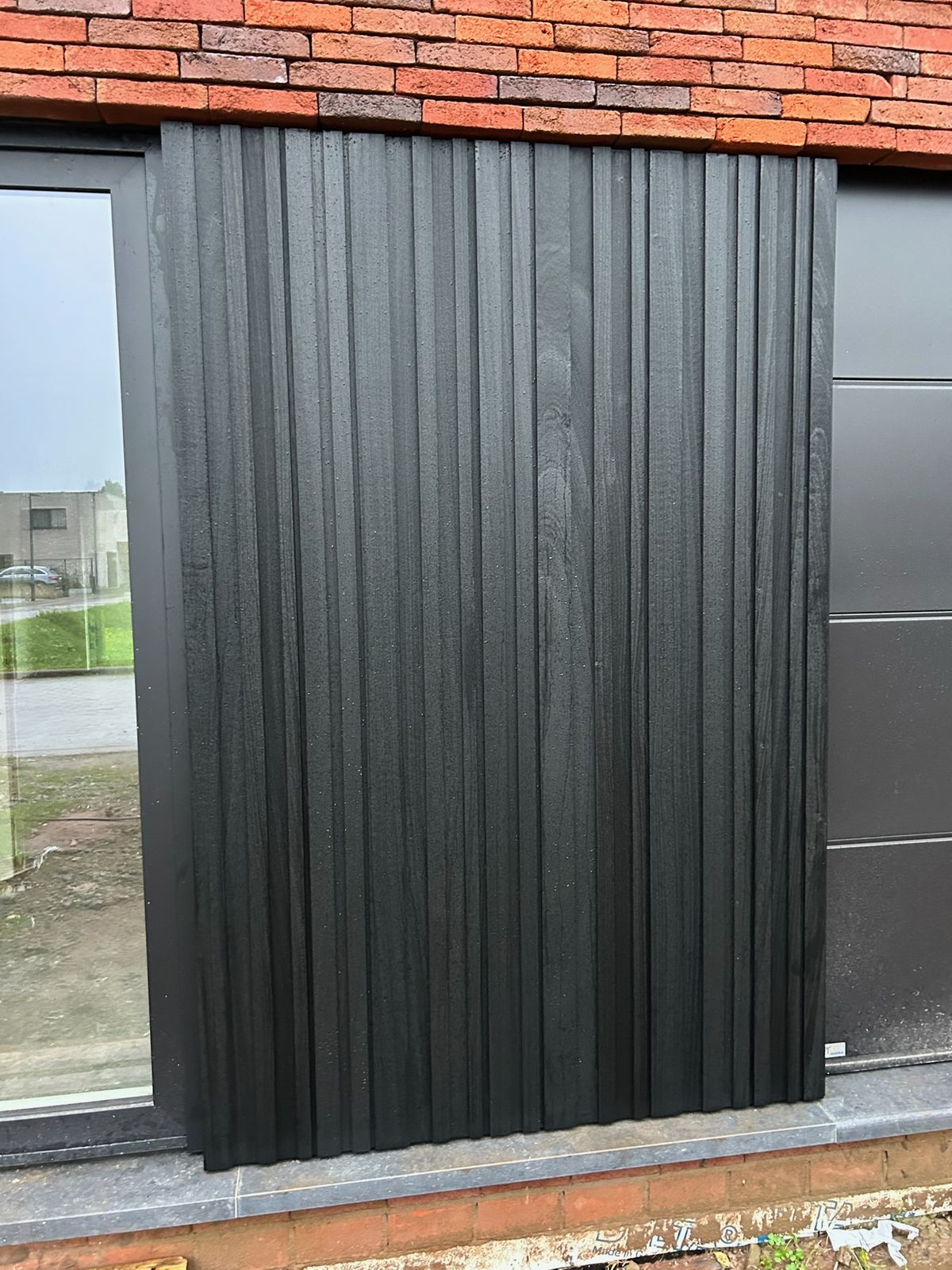 Detail van zwarte verticale gevelplanken naast een raam en zwarte panelen in Wingene.