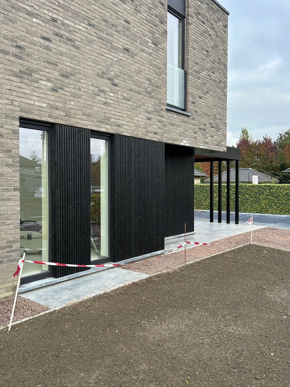 Zwarte gevelbekleding op het gelijkvloers onder een grijze bakstenen verdieping in Wijnendale.