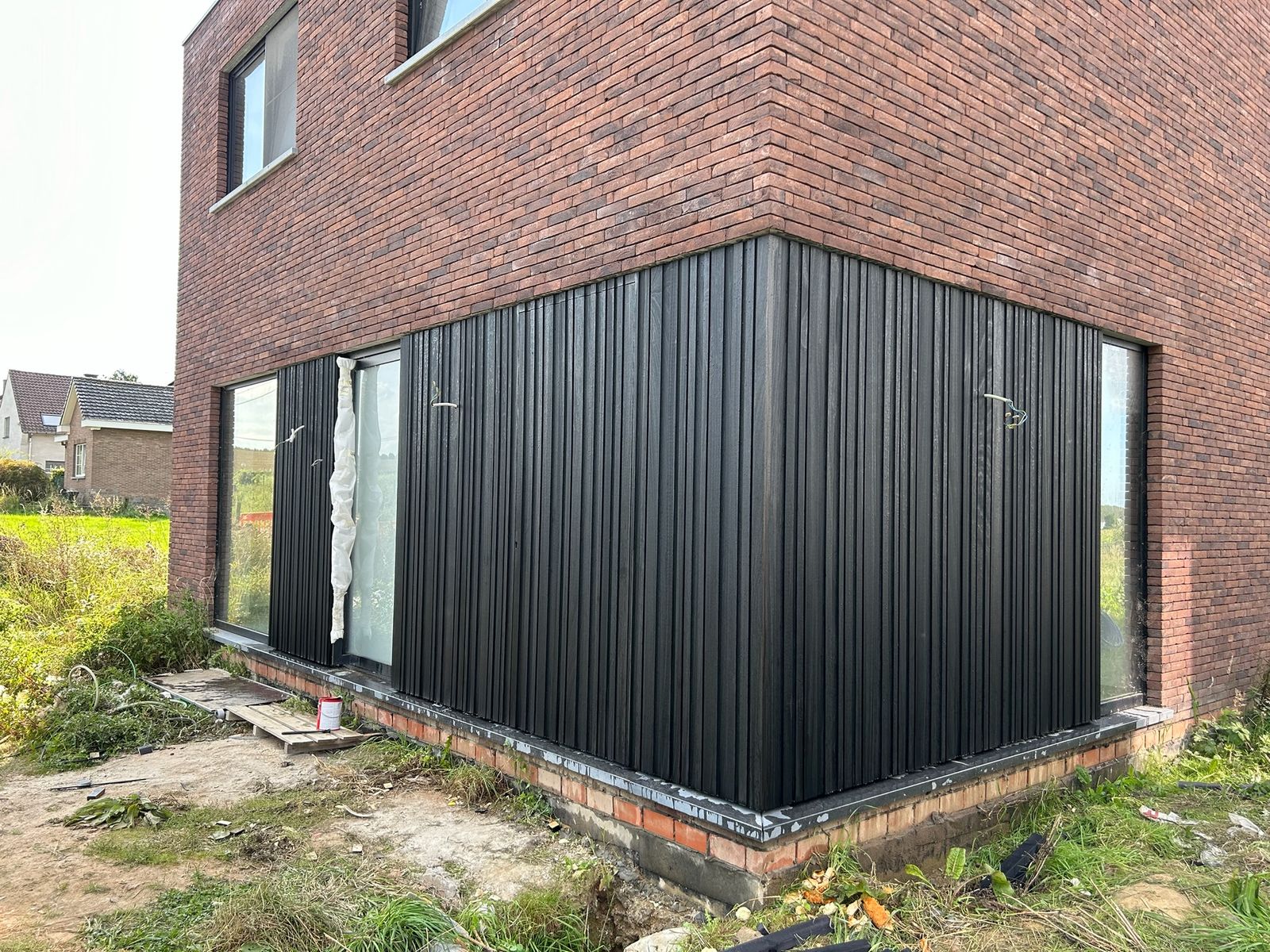 Zwarte verticale gevelbekleding rond de hoek van een bakstenen woning in Wambeek.