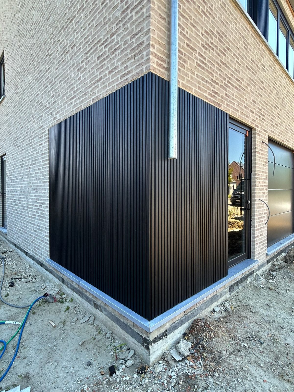 Zwarte gevelbekleding op de hoek van een nieuwbouwwoning in lichte baksteen in Torhout.