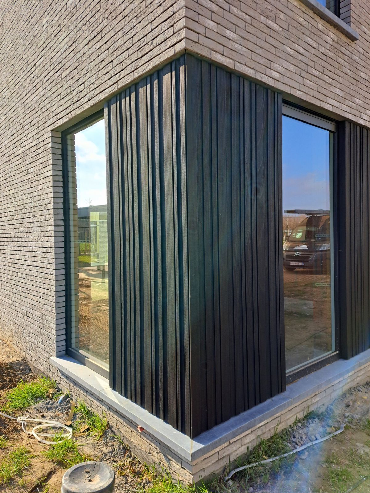 Zwarte verticale gevelbekleding rond een hoekraam van een nieuwbouwwoning in Herzele.
