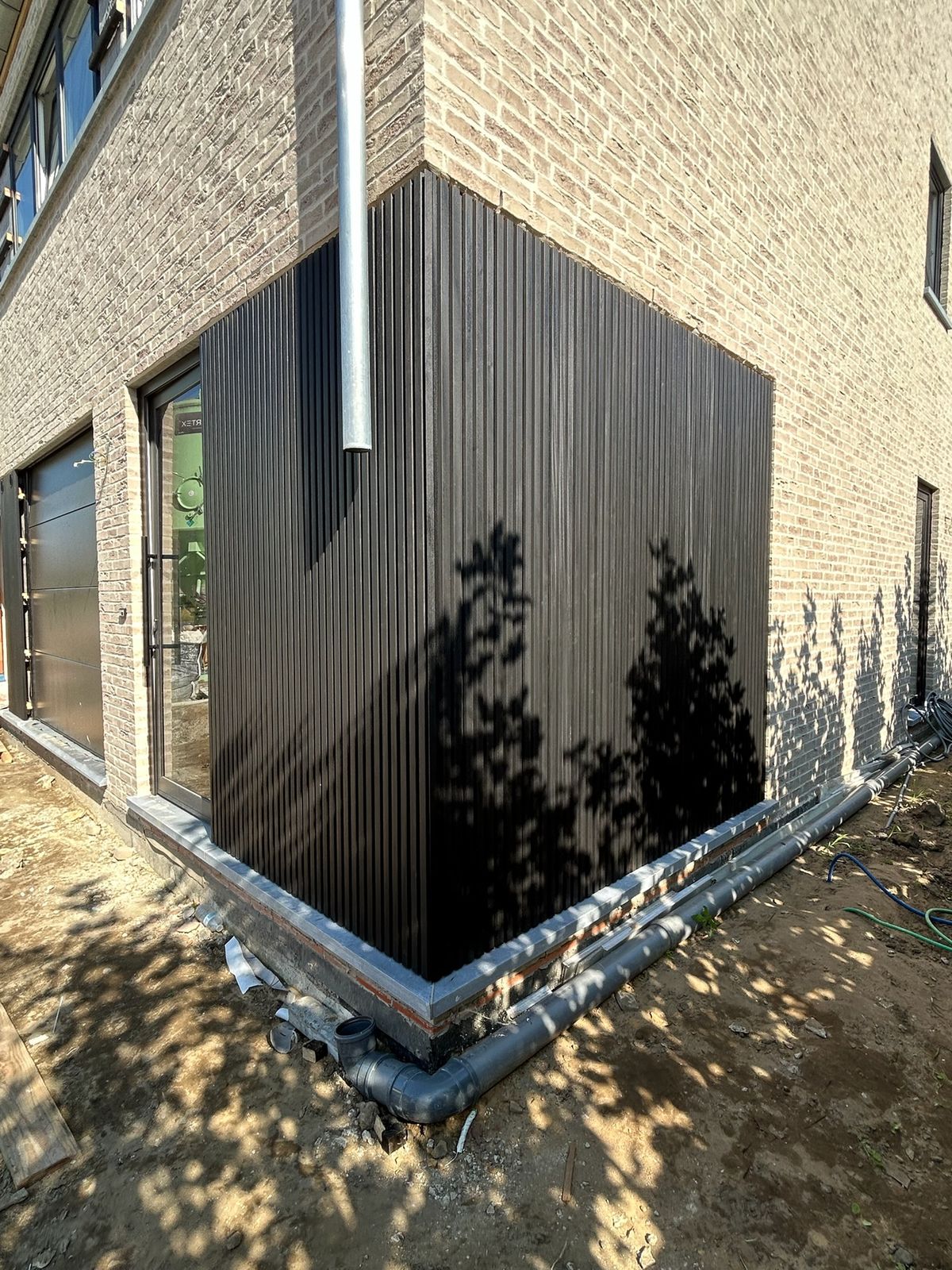 Detail van de hoekafwerking van zwarte gevelbekleding in de zon in Torhout.