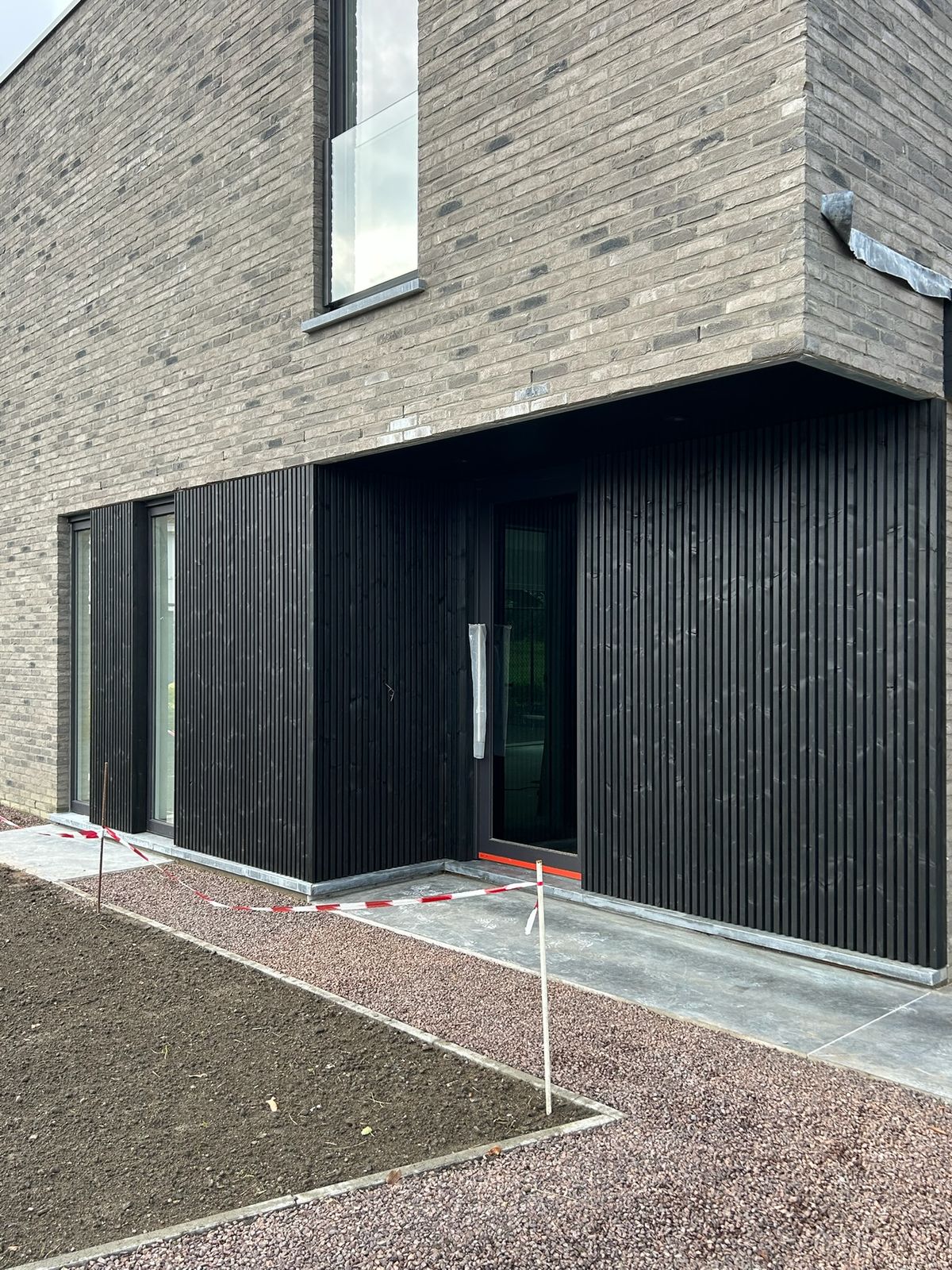 Zwarte verticale gevelbekleding rond de inkom van een nieuwbouwwoning in Wijnendale.