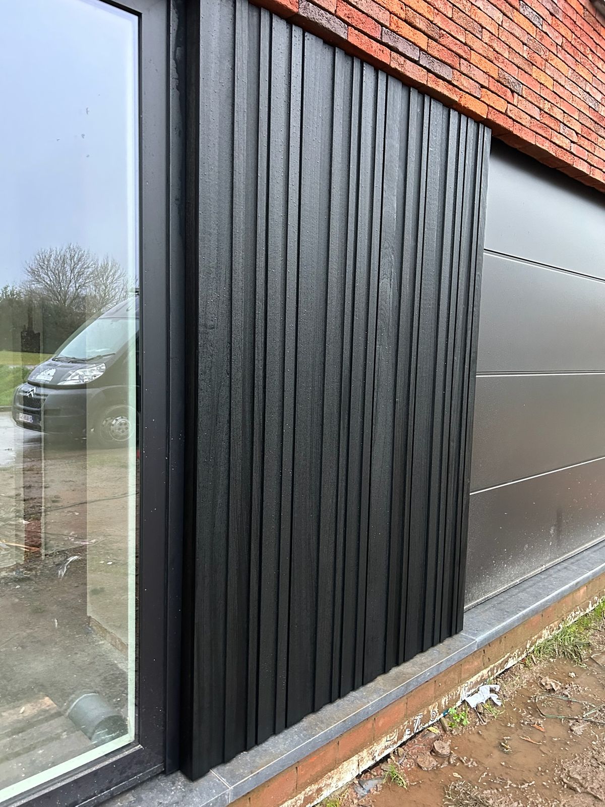 Zwarte gevelbekleding aansluitend op een raam en gevelpanelen van een woning in Wingene.