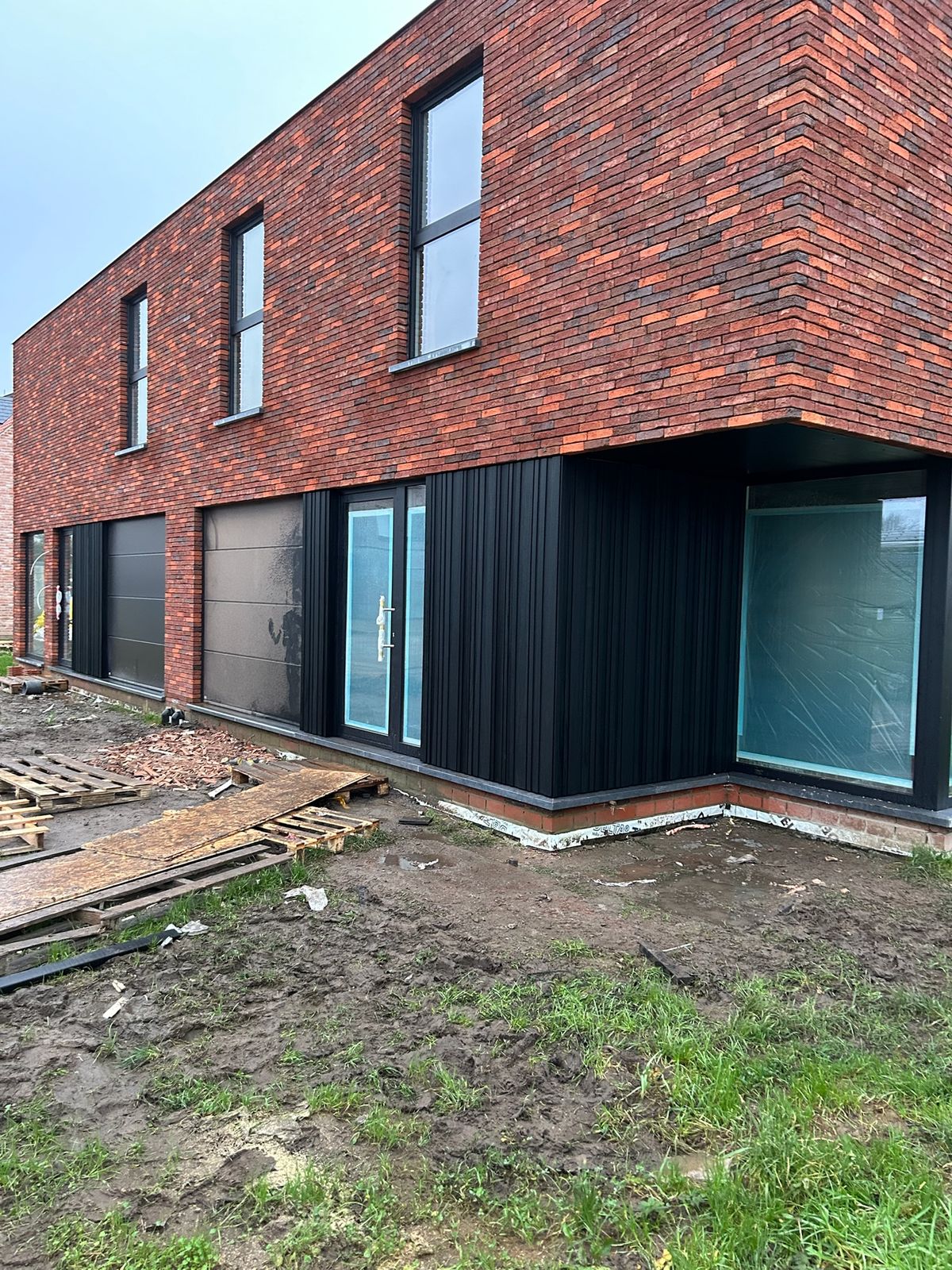 Nieuwbouw in rode baksteen met zwarte gevelbekleding op de benedenverdieping in Wingene.
