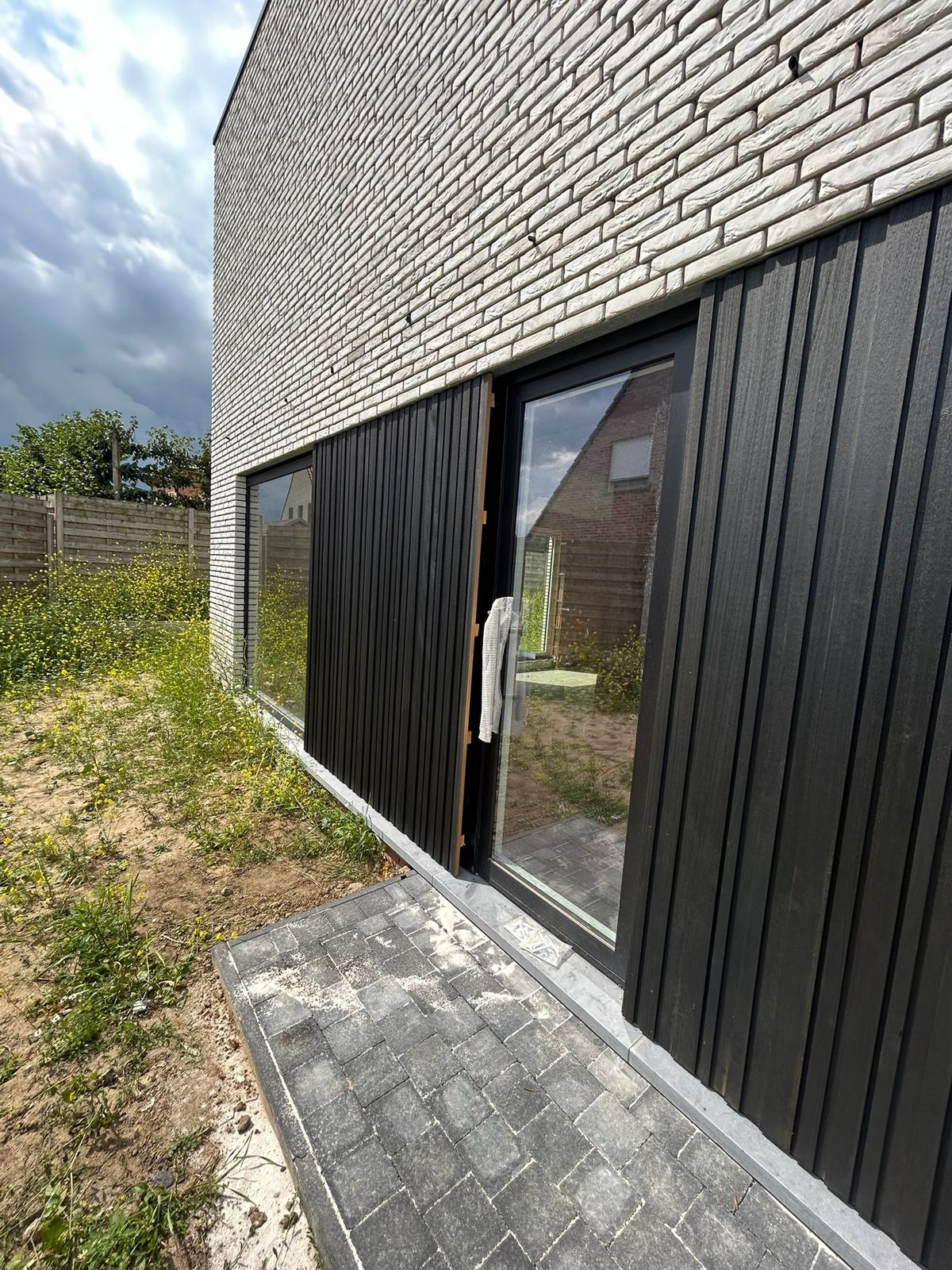 Zwarte verticale gevelbekleding rond een schuifraam van een nieuwbouwwoning in Kortemark.
