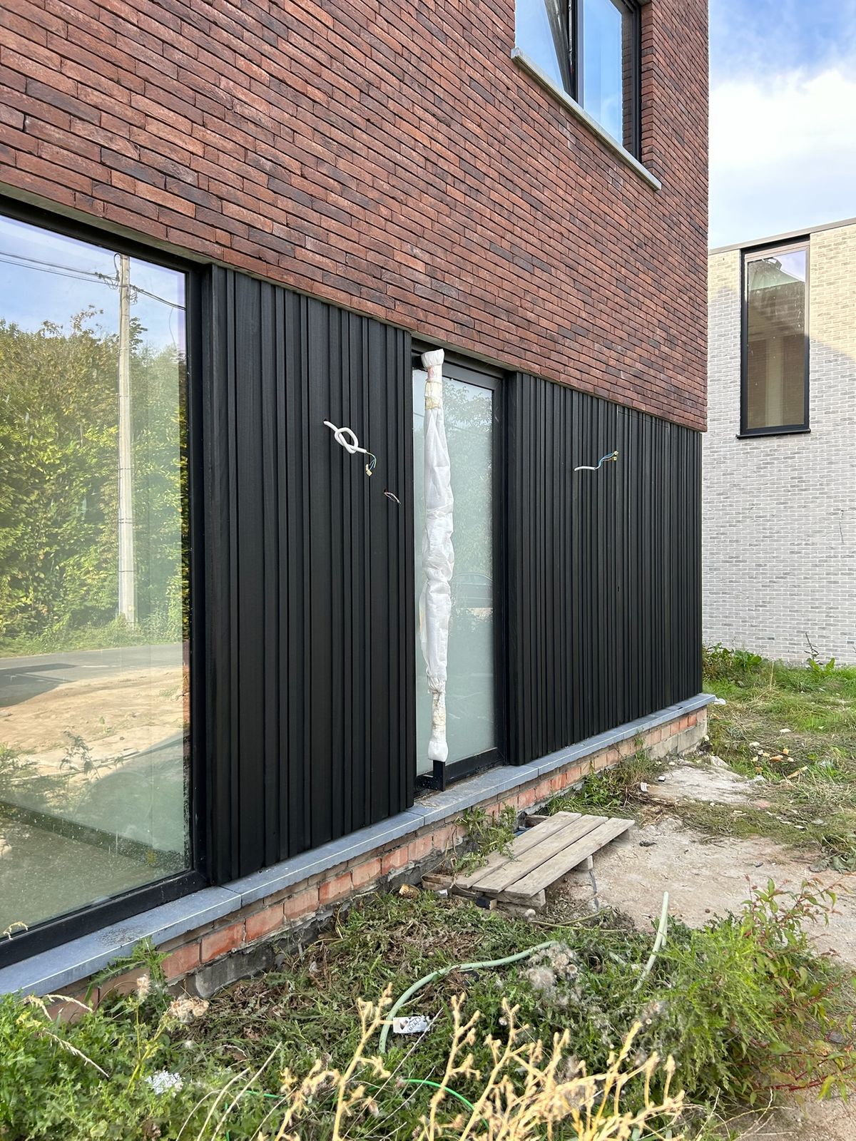 Zijgevel met zwarte gevelbekleding tussen grote ramen onder rode baksteen in Wambeek.
