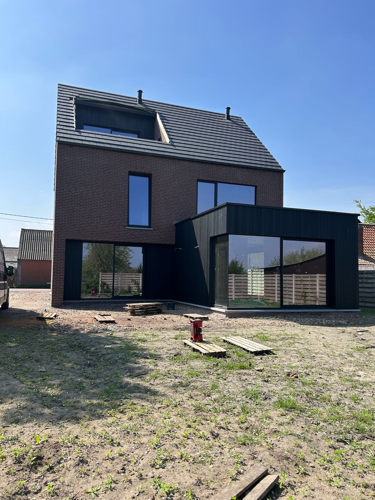 Bakstenen woning met zwarte houten aanbouw en grote ramen aan de achterzijde in Maldegem.