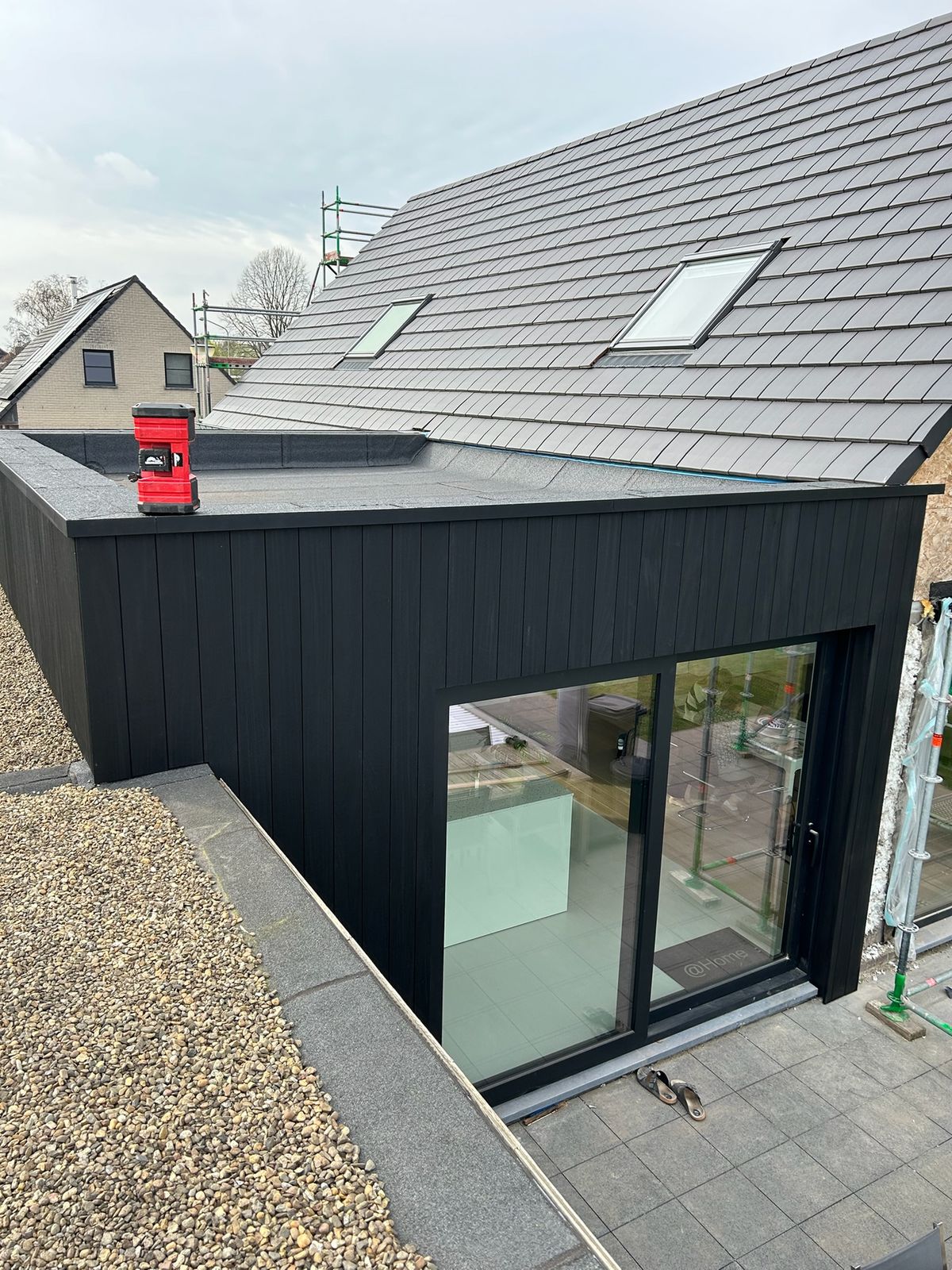 Zwarte houten aanbouw met schuifraam onder een pannendak met dakramen in Teralfene.