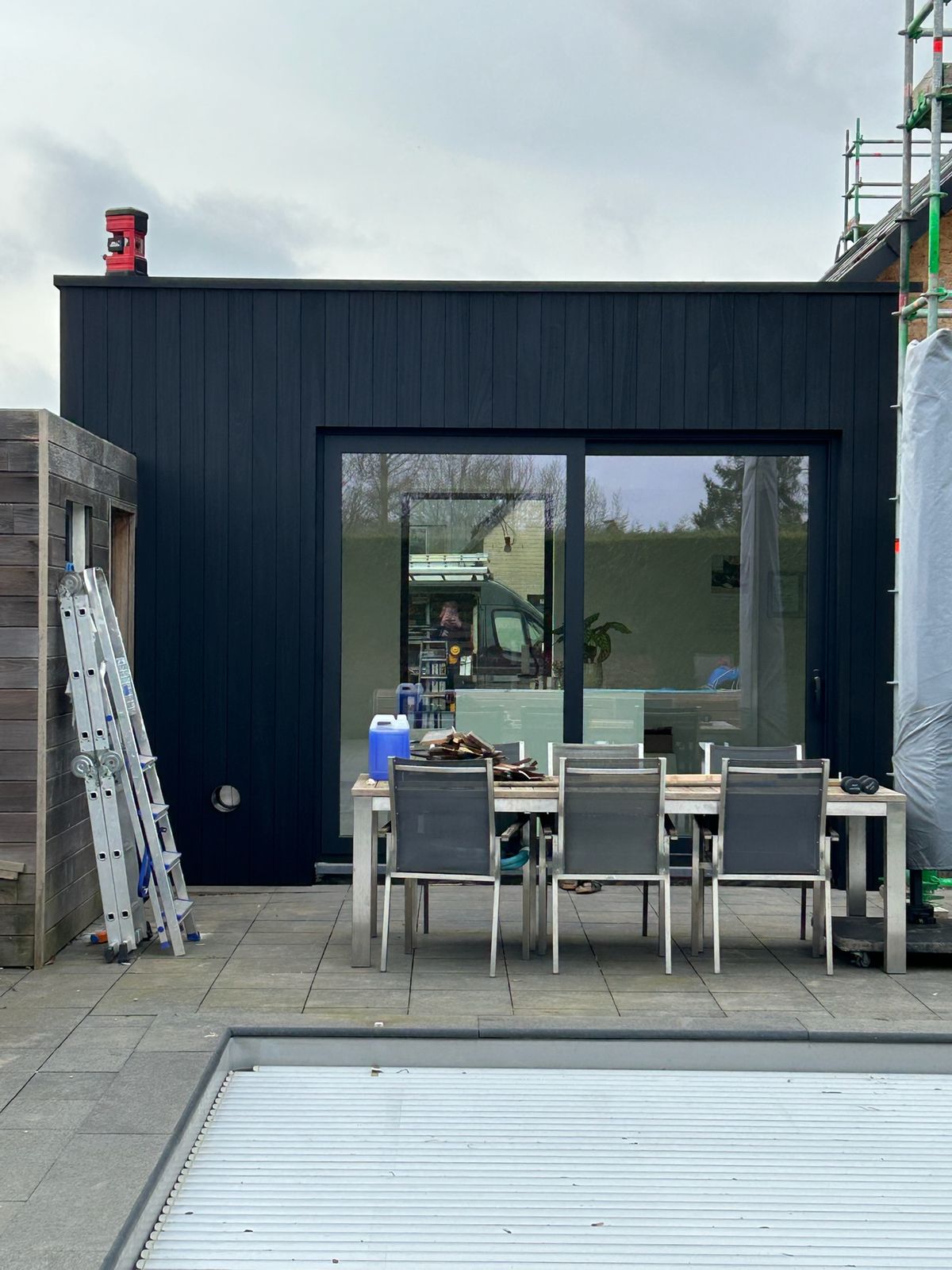 Zwarte houten aanbouw met groot schuifraam aan een terras in Teralfene.