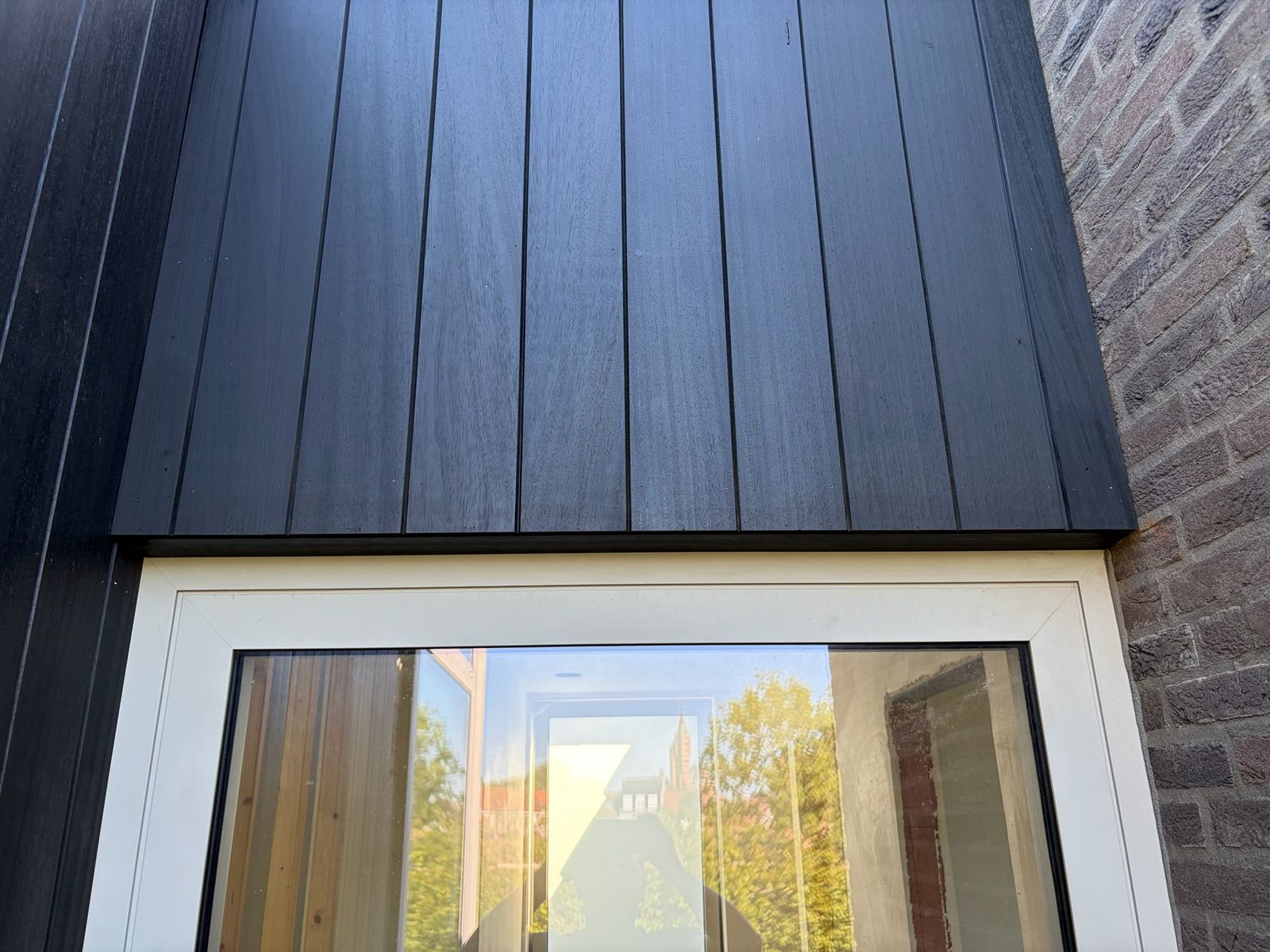 Zwarte houten gevelbekleding in verticale planken boven een groot wit raam in Sint-Kruis.