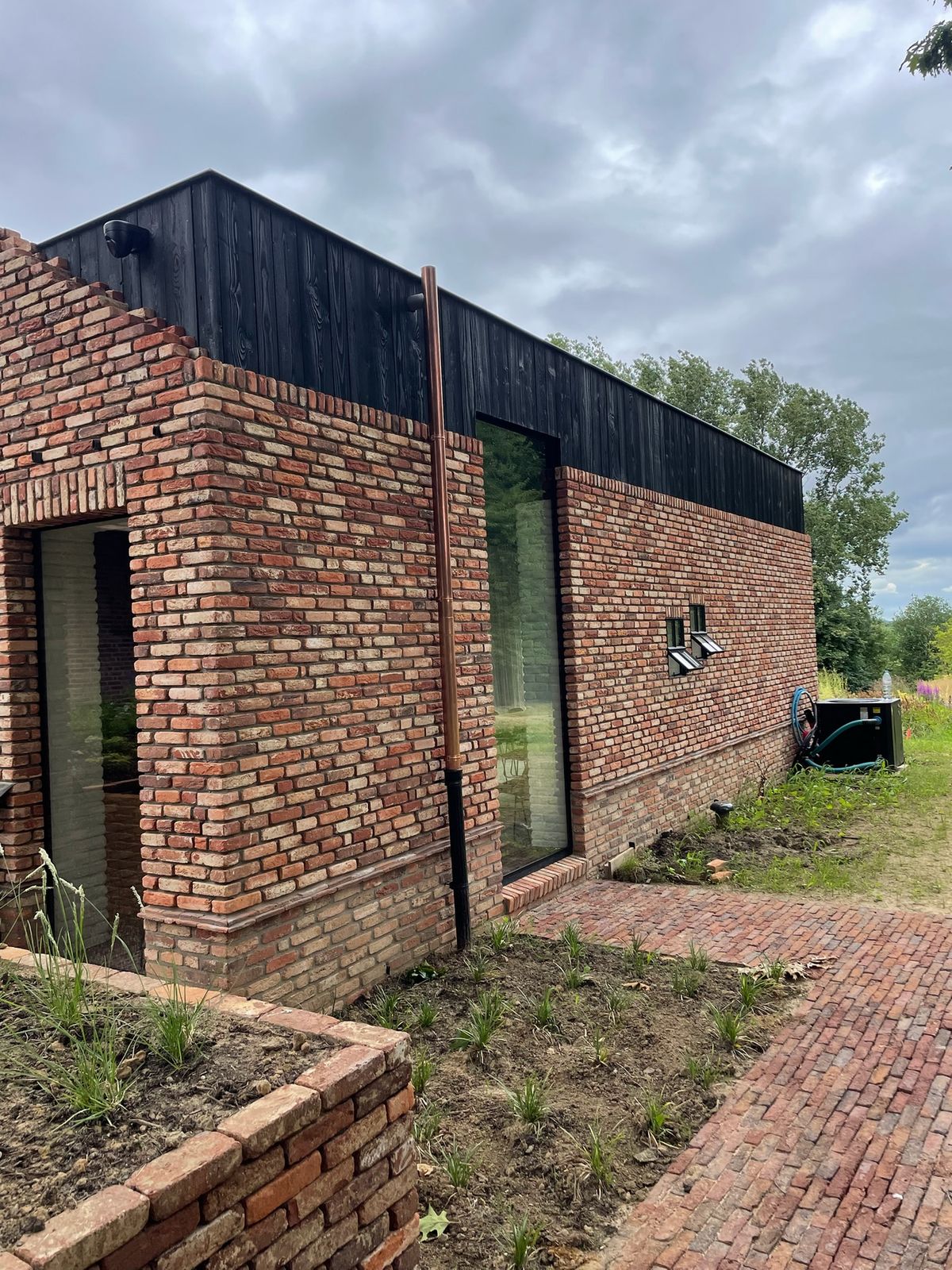 Zwarte houten gevelbekleding boven een gevel in rode baksteen in Meise.