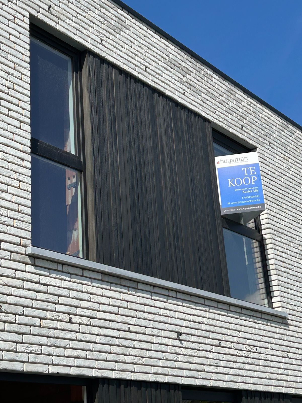 Detail van zwarte houten gevelbekleding naast een raam in een grijze gevel in Kortemark.