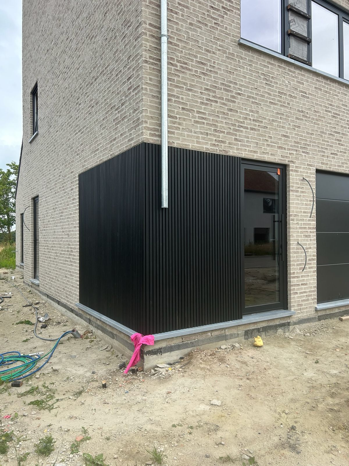 Hoek van een woning met zwarte verticale gevelbekleding en lichte baksteen in Torhout.