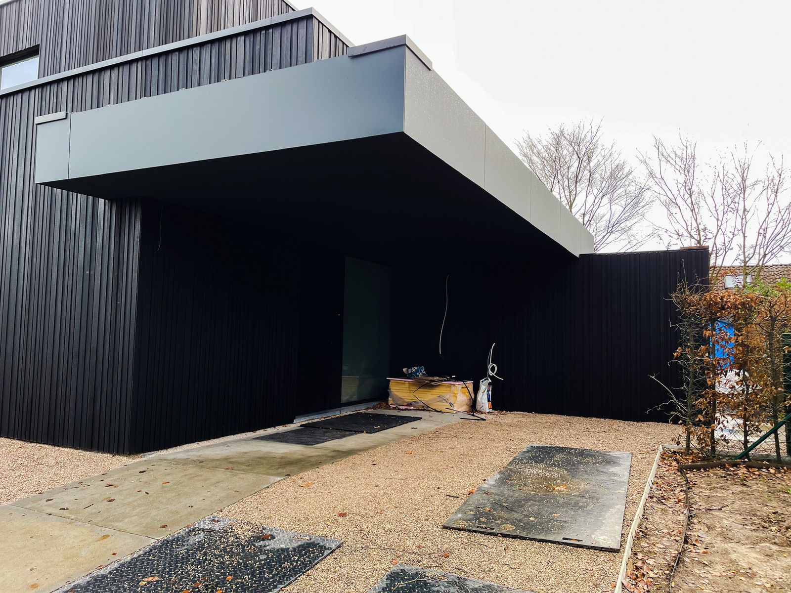 Zwarte houten gevel met grote uitkragende luifel boven de inkom in Overijse.