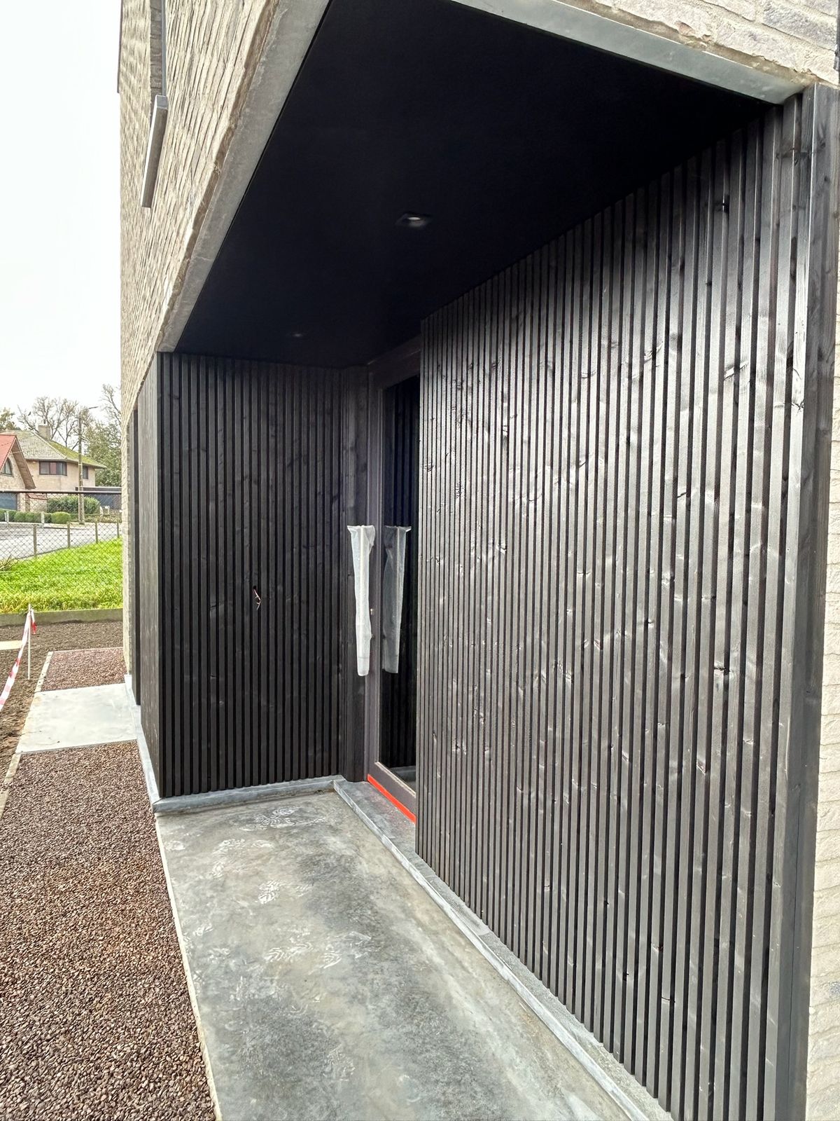 Zwarte houten gevelbekleding in een overdekte inkomzone van een woning in Wijnendale.