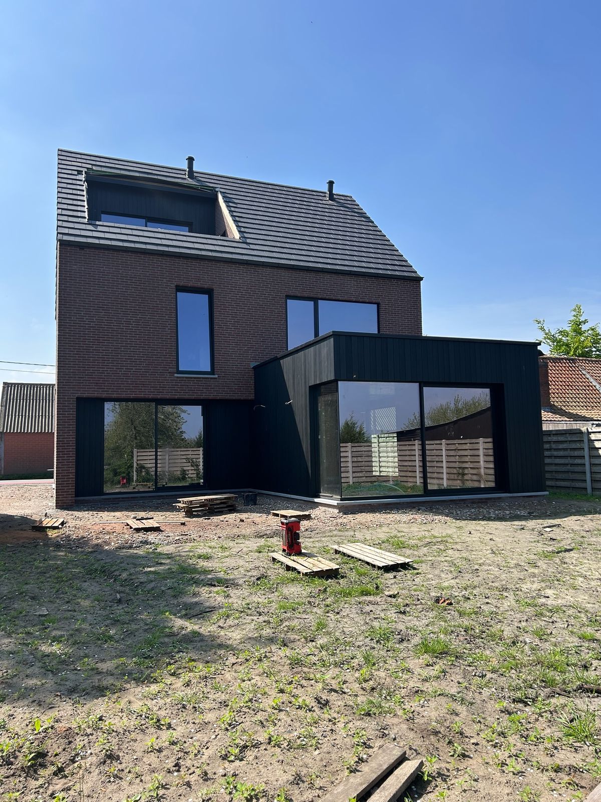 Achtergevel met zwarte houten gevelbekleding op de gelijkvloerse aanbouw van een woning in Maldegem.
