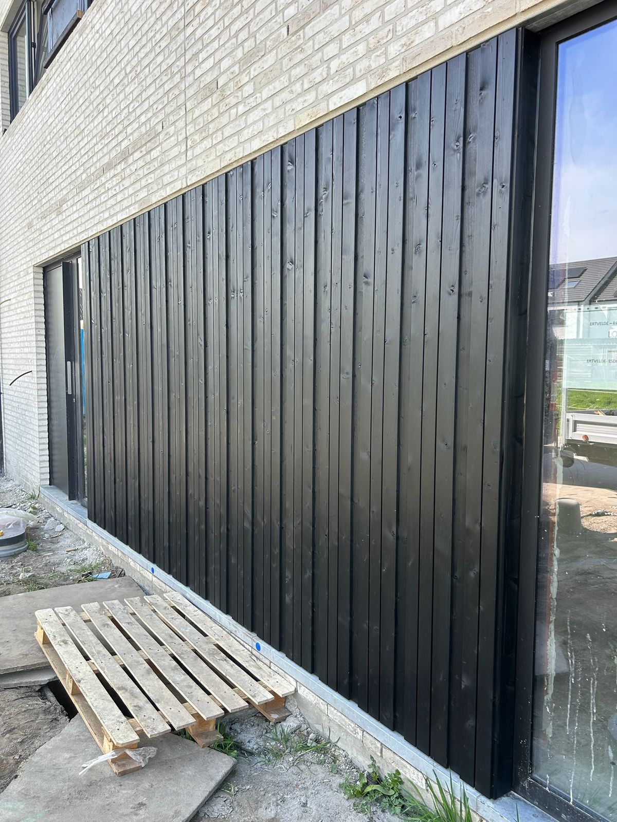 Zwarte verticale houten gevelbekleding naast een groot raam in een witte bakstenen gevel in Rieme.