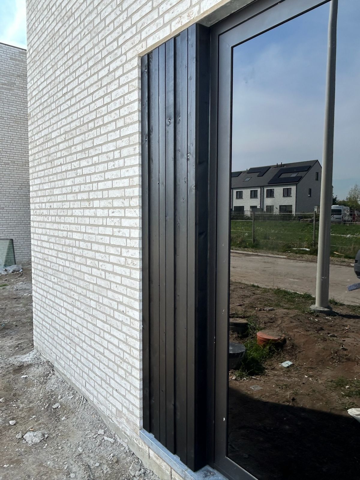 Zwarte houten gevelbekleding naast een hoog raam in een witte bakstenen gevel in Rieme.