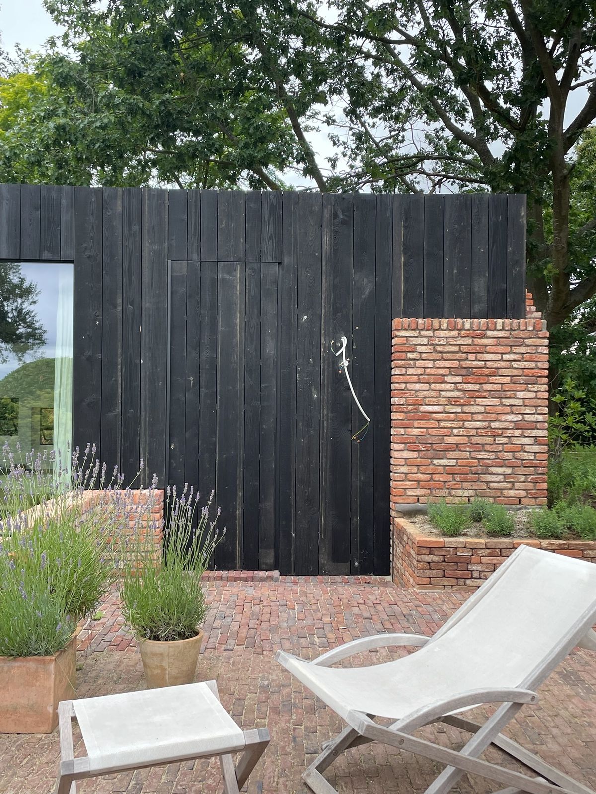 Zwarte houten gevelbekleding bij een terras met bakstenen muurtjes in de tuin in Meise.