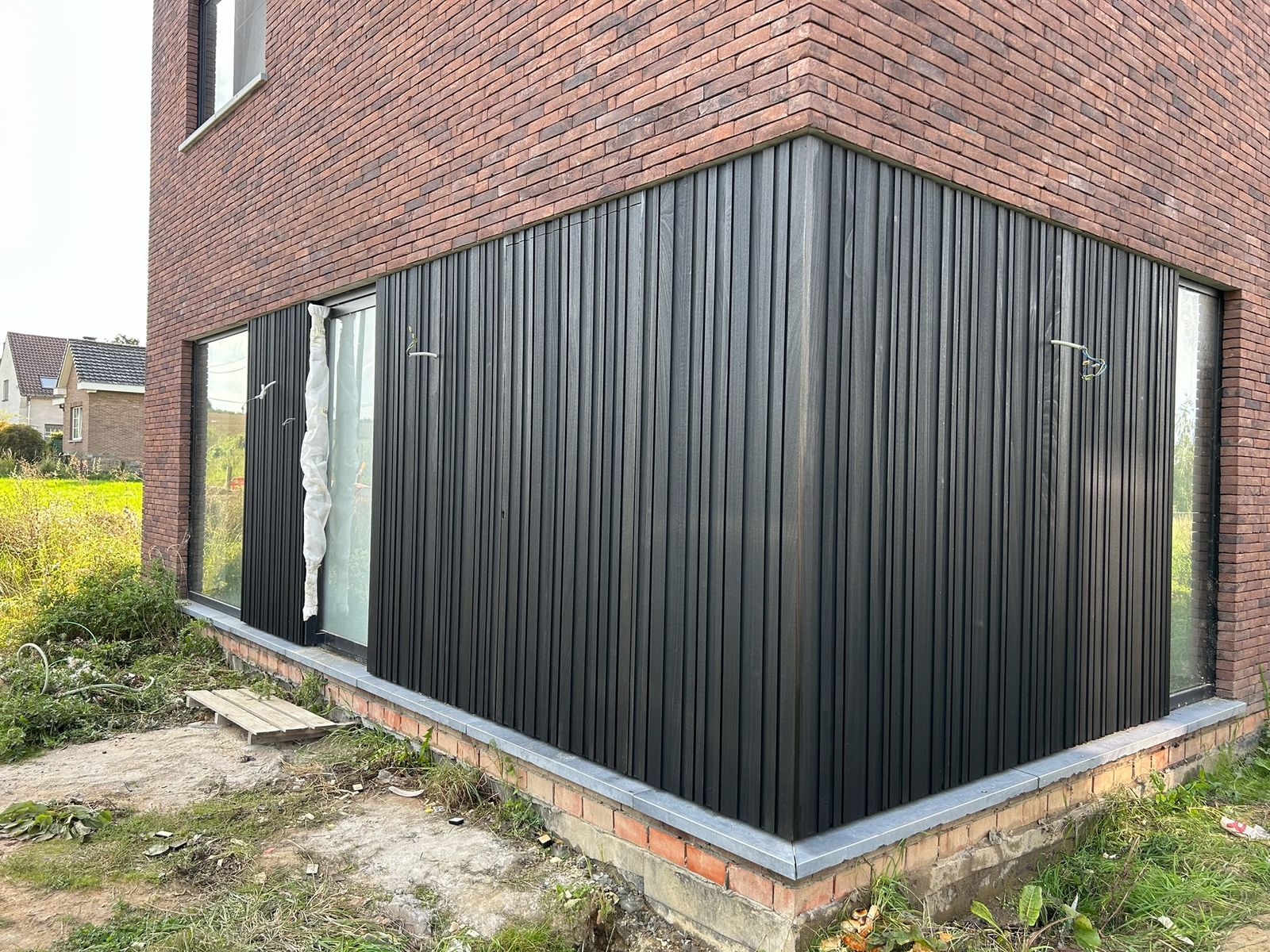 Zwarte houten gevelbekleding op de benedenverdieping van een bakstenen nieuwbouw in Wambeek.