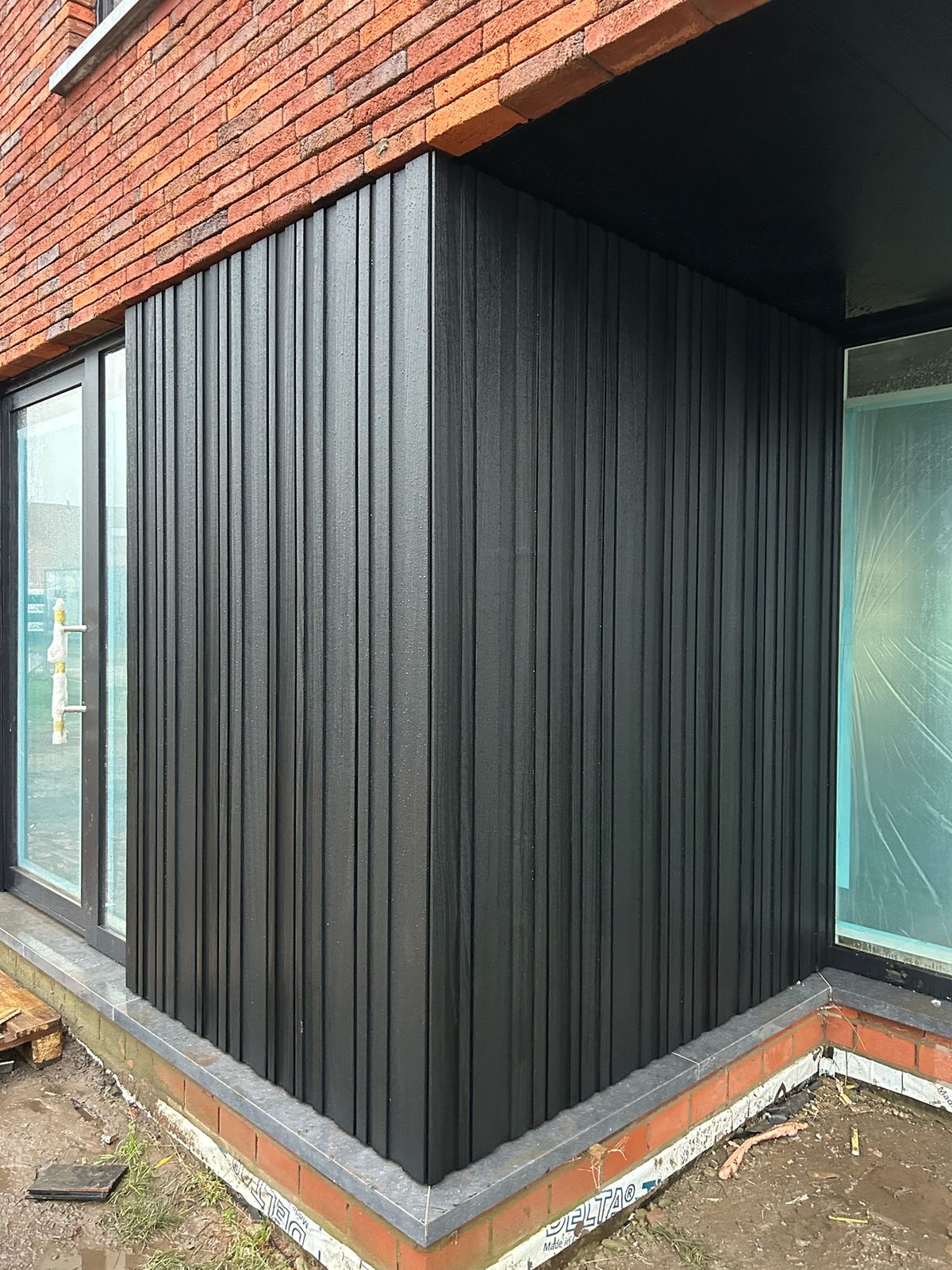 Zwarte verticale gevelbekleding tussen twee grote ramen van een nieuwbouw in Wingene.