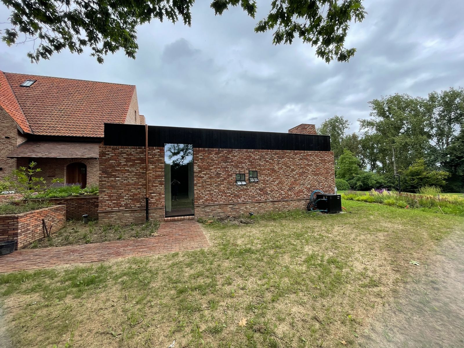 Bakstenen woning met zwarte houten gevelbekleding onder de dakrand in een grote tuin in Meise.