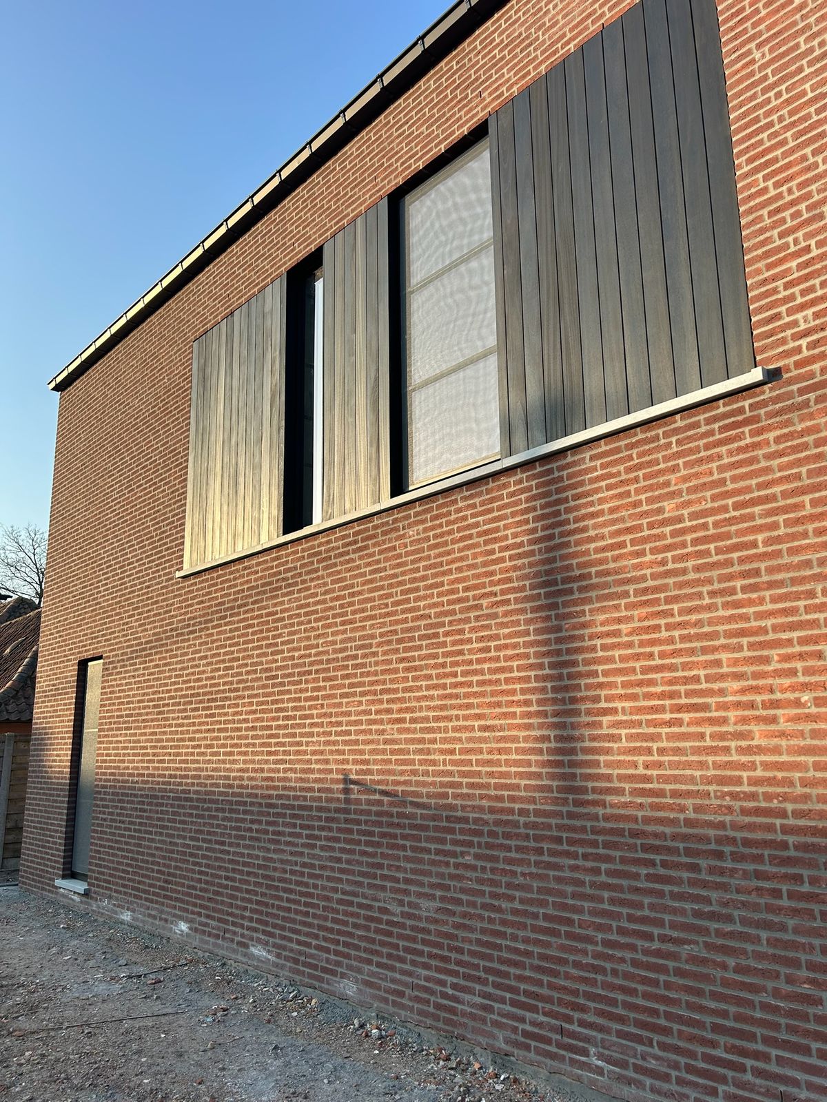 Bakstenen zijgevel met zwarte houten panelen naast de ramen op de verdieping in Maldegem.