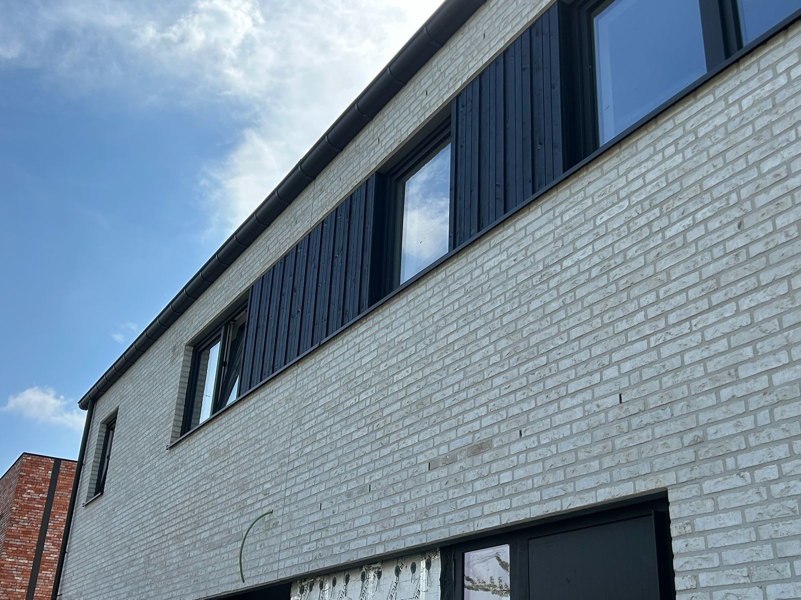 Strook zwarte houten gevelbekleding langs de ramen van een witte nieuwbouw in Rieme.
