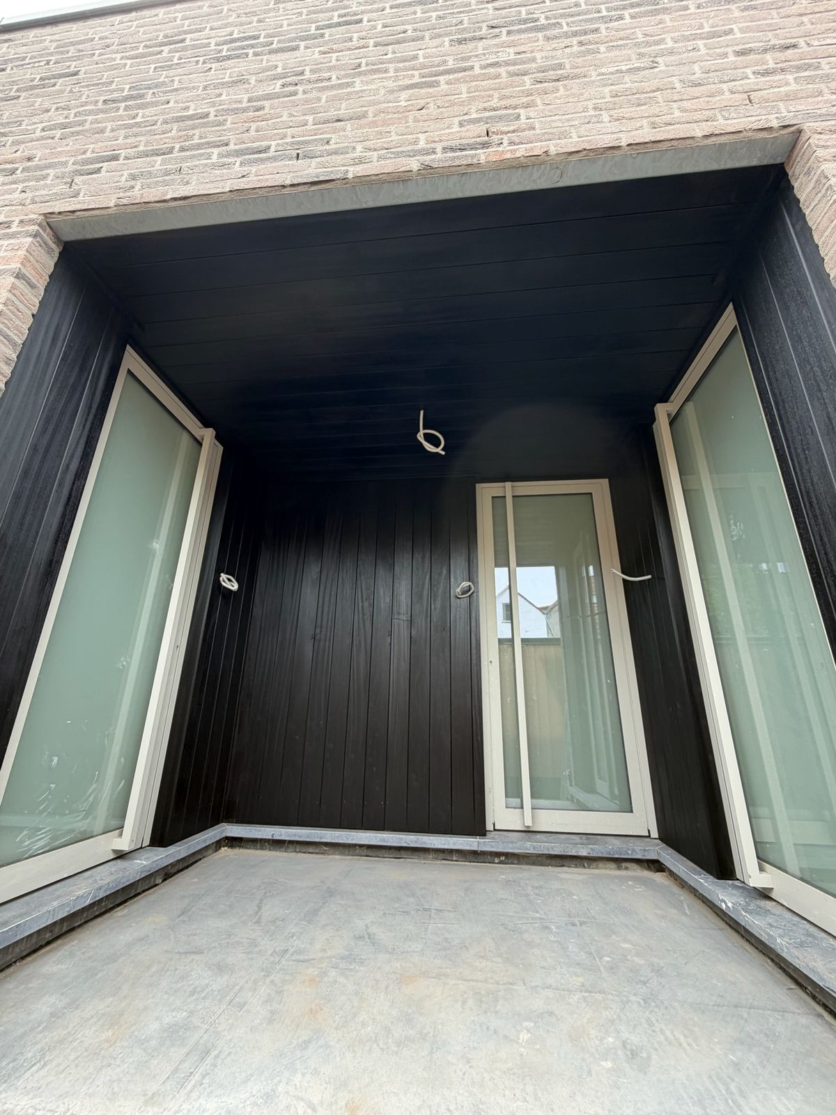 Loggia met zwart houten plafond en zwarte wandbekleding tussen twee glazen deuren in Sint-Kruis.