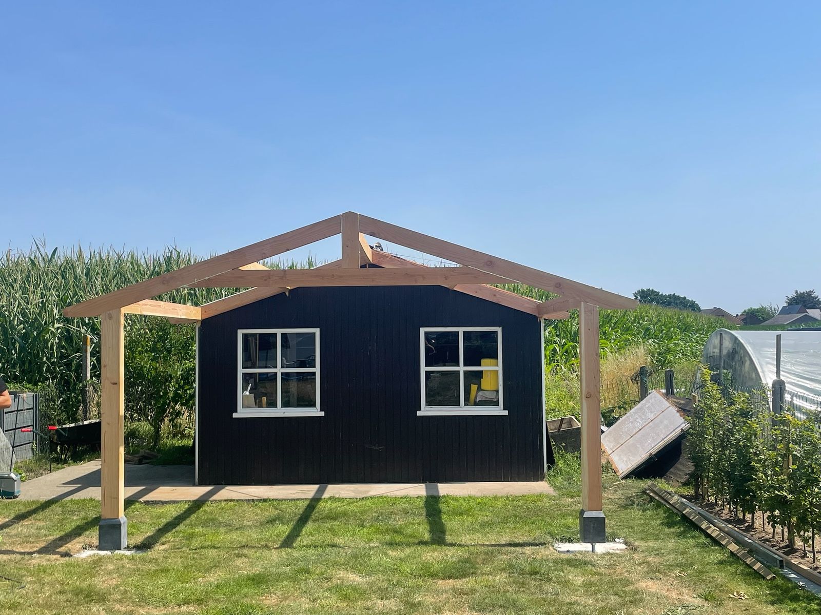 Zwart bekleed poolhouse met houten dakspanten in opbouw in een tuin in Machelen.