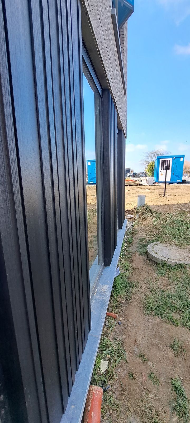 Zijzicht op zwarte verticale gevelplanken langs een raam van een woning in Herzele.